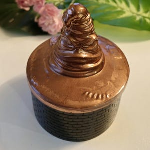 May include: A set of three ceramic mugs with a speckled, matte finish. The mugs are in shades of cream, light brown, and dark brown. Each mug has a rounded handle and a simple, minimalist design.