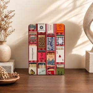 May include: A rectangular tray featuring a collage of various vintage matchbox designs. The print includes diverse graphics such as a leopard print, a cityscape, playing cards, and brand logos like Hermes, all arranged on a red and white striped background.