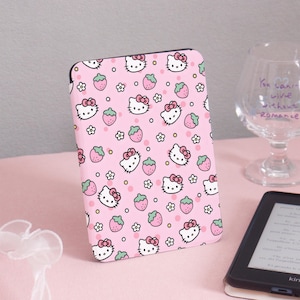 Op de afbeelding: Een roze e-reader hoesje met een herhalend patroon van Hello Kitty gezichten, aardbeien en bloemen. De hoes is ontworpen voor een rechthoekig e-reader apparaat. Het ontwerp bevat witte, roze en groene kleuren.