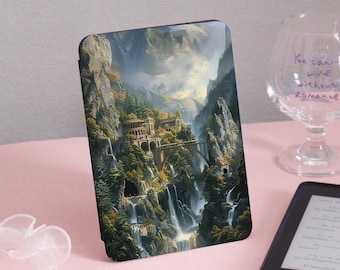 May include: A tablet case featuring a detailed landscape painting of a mountain valley with waterfalls, bridges, and buildings. The artwork is in shades of green, brown, and blue, with a bright sky. The case is on a pink surface.