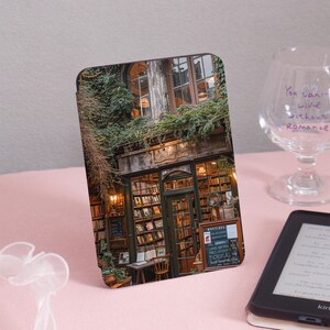 Puede incluir: Una librería de estilo vintage con un toldo verde y un letrero que dice "OLIVER'S BOOKS". La fachada está cubierta de hiedra y tiene un gran escaparate de libros. Hay una mesa de madera y sillas fuera de la tienda.