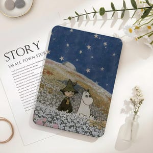 May include: A rectangular, illustrated case featuring a whimsical scene with a starry night sky, a character in a green hat and cloak, and a white creature in a field of white flowers. The case has a blue background and is likely for a tablet or phone.