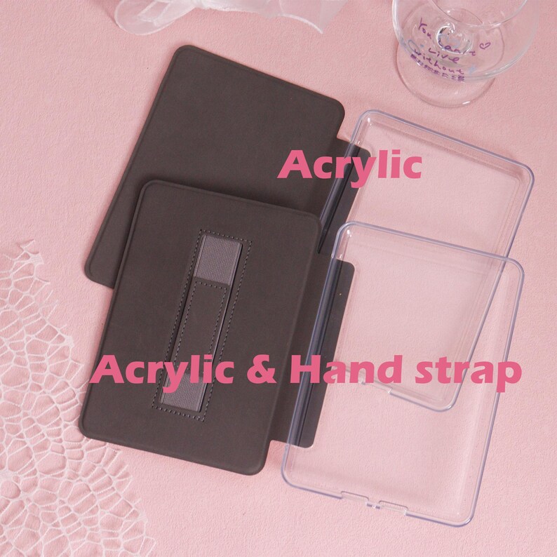 K&ouml;nnte beinhalten: Eine braune Tablet-H&uuml;lle aus Acryl mit Handschlaufe und einer transparenten Acrylabdeckung. Die Texte "Acrylic" und "Acrylic & Hand strap" sind sichtbar. Die H&uuml;lle liegt auf einer rosa Oberfl&auml;che.