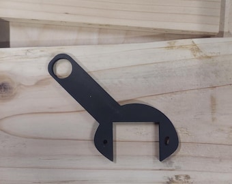 May include: A black, metal spanner wrench with a circular opening and a square-shaped head. The tool is designed for tightening or loosening nuts and bolts. The wrench is set against a light-colored wooden background.