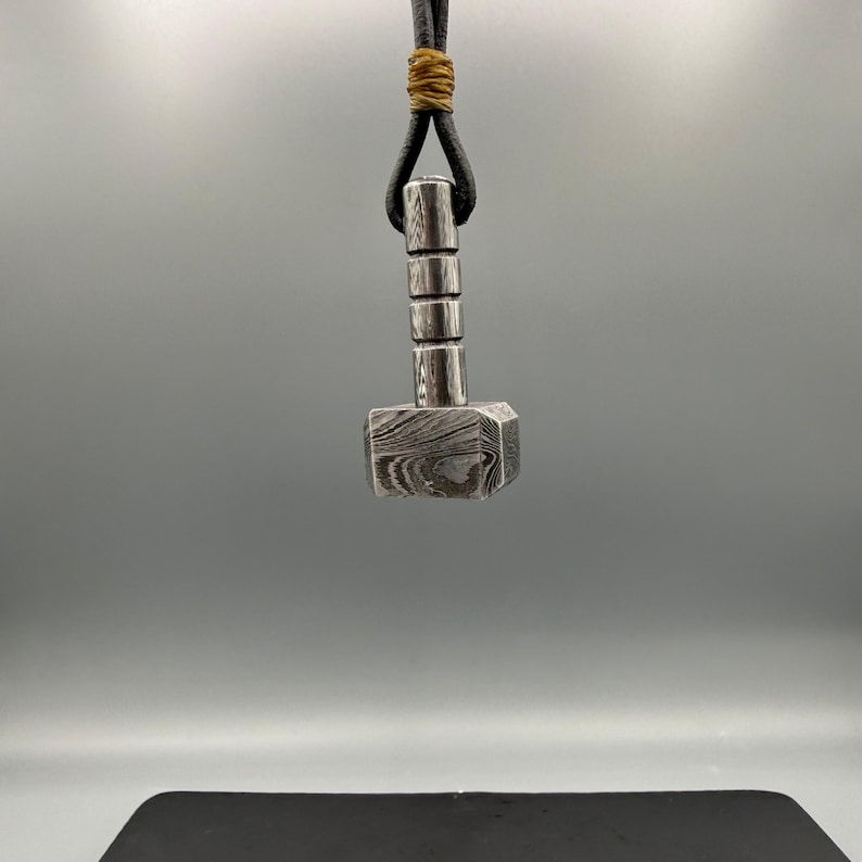 Hand-forged Mjölnir pendant made from premium Damascus steel, showcasing intricate layered steel patterns and a bold hammer-of-Thor design. This striking men’s norse pendant blends ancient mythology with modern metal craftsmanship and is perfect for everyday wear or as a statement piece for history-and-mythology lovers.