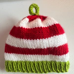 May include: A red and white striped knitted hat with a green pom-pom on top. The hat has a green brim.