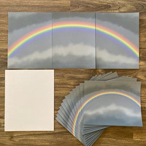 May include: A set of 12 cards featuring a rainbow over a cloudy sky. The cards are gray with a rainbow in shades of red, orange, yellow, green, blue, indigo, and violet.