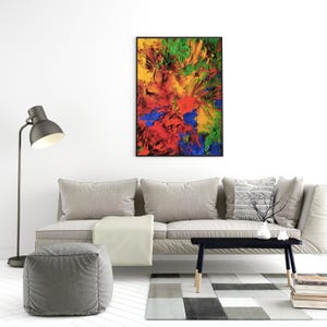 K&ouml;nnte beinhalten: Abstraktes Gem&auml;lde in einem schwarzen Rahmen mit einem farbenfrohen Design aus Rot, Gelb, Gr&uuml;n und Blau. Das Gem&auml;lde h&auml;ngt an einer wei&szlig;en Wand &uuml;ber einem grauen Sofa mit einer wei&szlig;en Wolldecke und einem grauen Hocker.