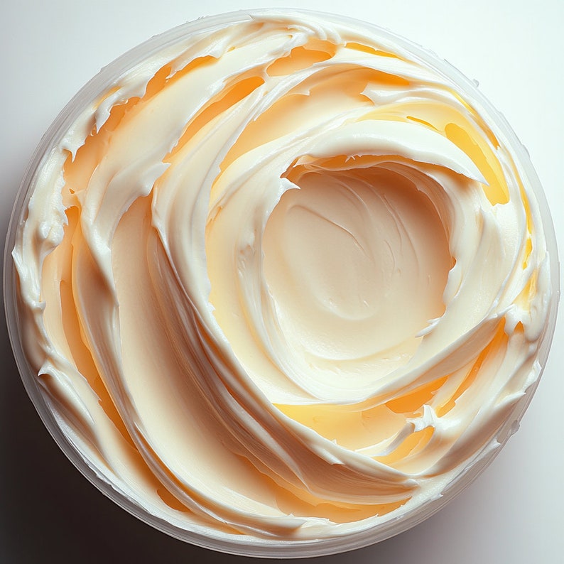 Puede incluir: Primer plano de un recipiente de mantequilla corporal blanca y cremosa. La mantequilla est&aacute; en espiral y es suave, con un tono amarillo claro.