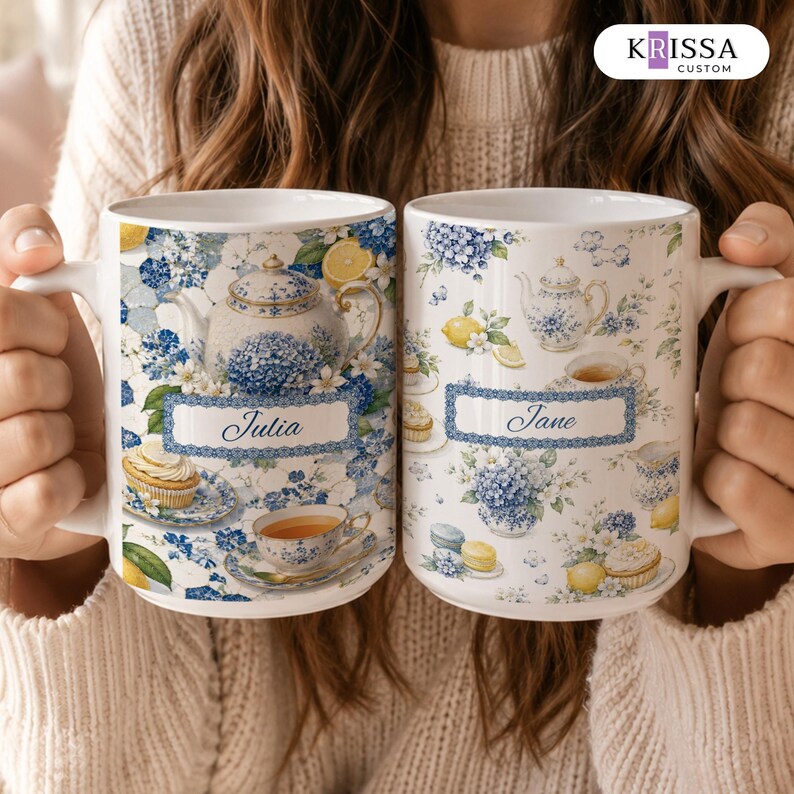 May include: Two white ceramic mugs featuring a blue and white floral pattern with illustrations of teapots, teacups, lemons, and cupcakes. The left mug displays the name Julia in a blue rectangular frame, and the right mug displays the name Jane.