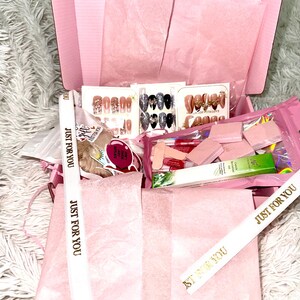 Peut inclure: Une bo&icirc;te cadeau rose remplie de divers accessoires pour nail art, notamment des ensembles de faux ongles, des limes &agrave; ongles et de l'huile &agrave; cuticules. La bo&icirc;te est doubl&eacute;e de papier de soie rose et contient des rubans avec l'inscription dor&eacute;e "JUST FOR YOU".