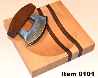 May include: A wooden cutting board with a curved well and three black walnut strips. A curved, stainless steel knife with a wooden handle is resting on the board. Item 0101.