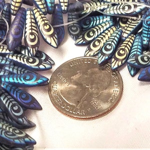 May include: A close-up of a pile of blue, white, and yellow ceramic beads with a swirling pattern. The beads are shaped like teardrops and are about the size of a US quarter.