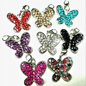 May include: Assortment of eight butterfly charms with rhinestone embellishments. Each charm features a different color, including red, gold, blue, black, purple, silver, pink, and multi-colored.
