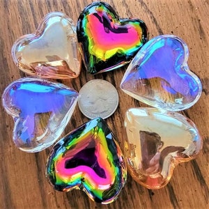 May include: Six iridescent glass heart-shaped ornaments in various colors, including pink, purple, blue, and green. The hearts are arranged in a circle on a wooden surface.
