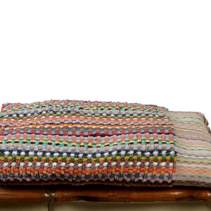 May include: A colorful striped and patterned bath towel with fringe on the ends. The towel is folded and placed on a wooden surface.