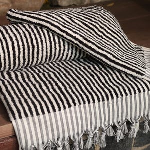 May include: Black and white striped Turkish towel with fringe. The towel is folded in half and has a white and black striped border.
