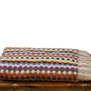 May include: A colorful striped and patterned bath towel with fringe on the edges. The towel is folded and placed on a wooden surface.