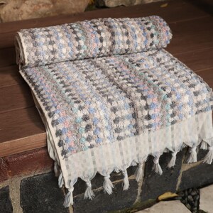 May include: A gray and white patterned Turkish towel with fringe. The towel is folded and laid out on a wooden surface.