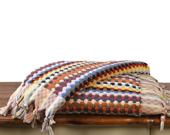 May include: A colorful patterned bath towel with fringe edges. The towel is folded in half and has a multi-colored geometric design.