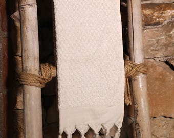 May include: A white cotton towel with fringe hanging on a wooden ladder. The ladder is made of bamboo and has a rustic look.