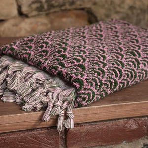 May include: A pink and green patterned Turkish towel with fringe. The towel is folded and has a decorative pattern.