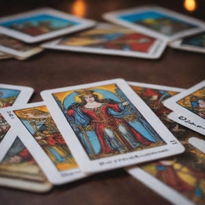 May include: A spread of tarot cards with a colorful illustration of a queen on the top card. The queen is wearing a red and blue robe and a crown. The card is labeled "The Empress".