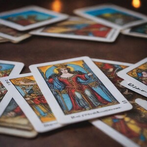 May include: A spread of tarot cards with a colorful illustration of a queen on the top card. The queen is wearing a red and blue robe and a crown. The card is labeled "The Empress".