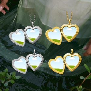 May include: Four heart-shaped lockets displayed in two silver-tone and two gold-tone finishes. Each locket is open, revealing a placeholder image of a green landscape under a blue sky. The lockets are attached to thin metal chains.