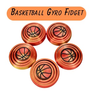 Puede incluir: Cinco juguetes fidget gyro de baloncesto rojos y dorados. Cada juguete tiene un diseño de baloncesto en el centro y el texto "Basketball Gyro Fidget" en una pancarta naranja encima de los juguetes.