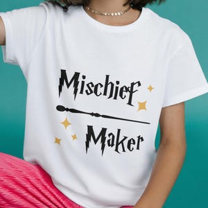 May include: White t-shirt with a black graphic that says "Mischief Maker" with a wand and lightning bolts.