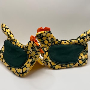 May include: Two chicken-shaped oven mitts. The mitts feature a black background with yellow lemons and green accents. The comb and wattle are orange. The mitts are designed to resemble chickens.