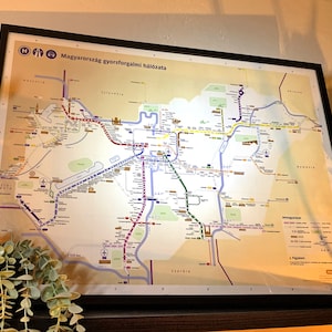 May include: A map of Hungary's public transportation system, showing the different lines and routes for trains, buses, and subways. The map is framed and hanging on a wall.