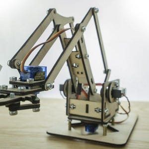 Pode incluir: Um kit de braço robótico de madeira com várias juntas e uma base. O braço tem um servo motor azul e é montado com parafusos. Um cartão com "Sky Labs" é segurado pelo braço.