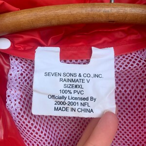 Puede incluir: Primer plano de un impermeable rojo con forro de malla blanca. Una etiqueta blanca muestra el texto "SEVEN SONS & CO., INC. RAINMATE V SIZE#XL 100% PVC Officially Licensed By 2000-2001 NFL MADE IN CHINA."