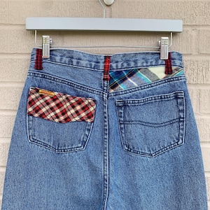 May include: Blue denim jeans with a plaid patch on the back pocket and a plaid waistband.