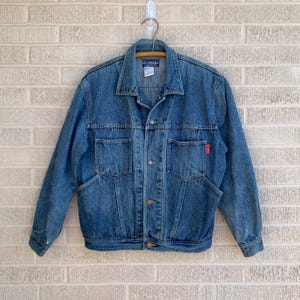 May include: A blue denim jacket with a red logo on the pocket. The jacket has a button closure and long sleeves.