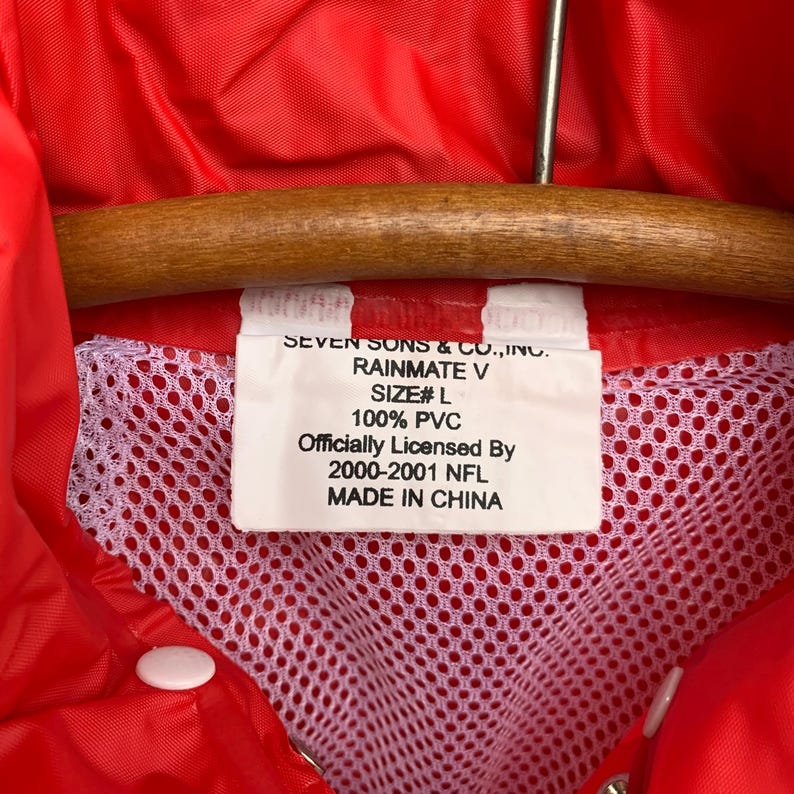 Puede incluir: Una chaqueta de lluvia roja con un forro de malla blanca. La etiqueta dice "Seven Sons & Co., Inc. Rainmate V Size# L 100% PVC Officially Licensed By 2000-2001 NFL Made in China."