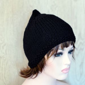 Op de afbeelding: Een zwarte gebreide beanie met een puntige top. De muts zit op een mannequinhoofd met kort bruin haar.