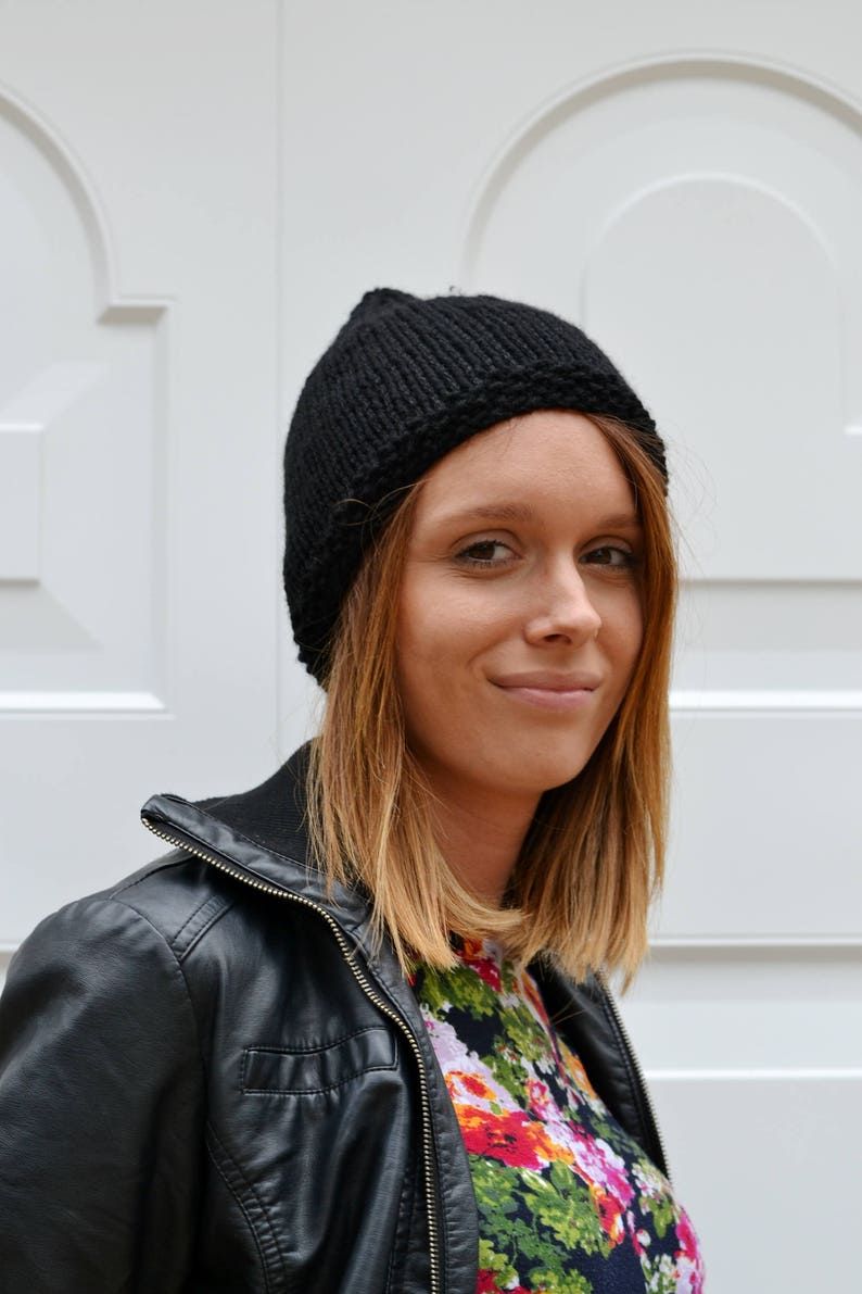 Op de afbeelding: Een vrouw draagt een zwart leren jack, een zwarte gebreide beanie en een shirt met bloemenprint.