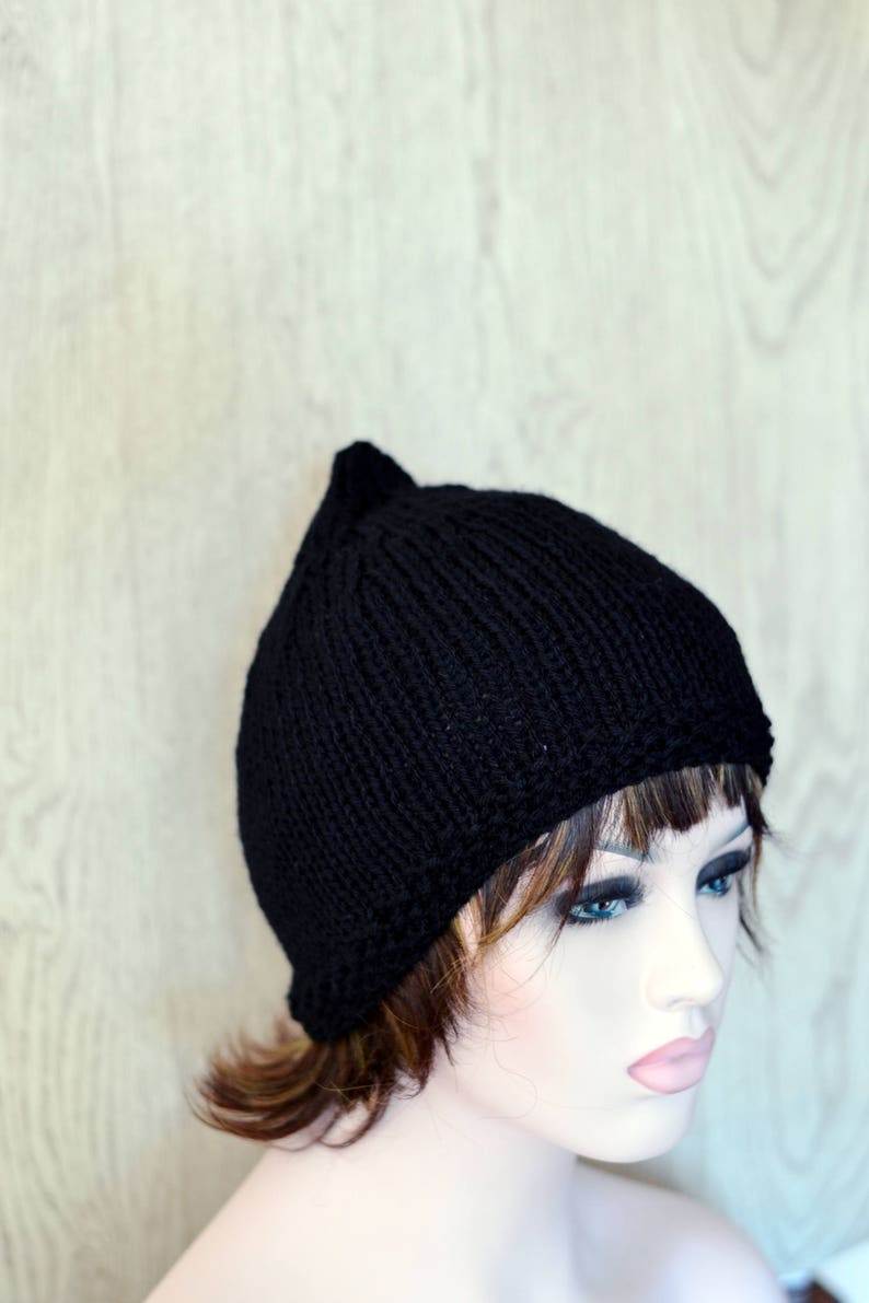 Op de afbeelding: Een zwarte gebreide beanie met een puntige top. De muts zit op een mannequinhoofd met kort bruin haar.