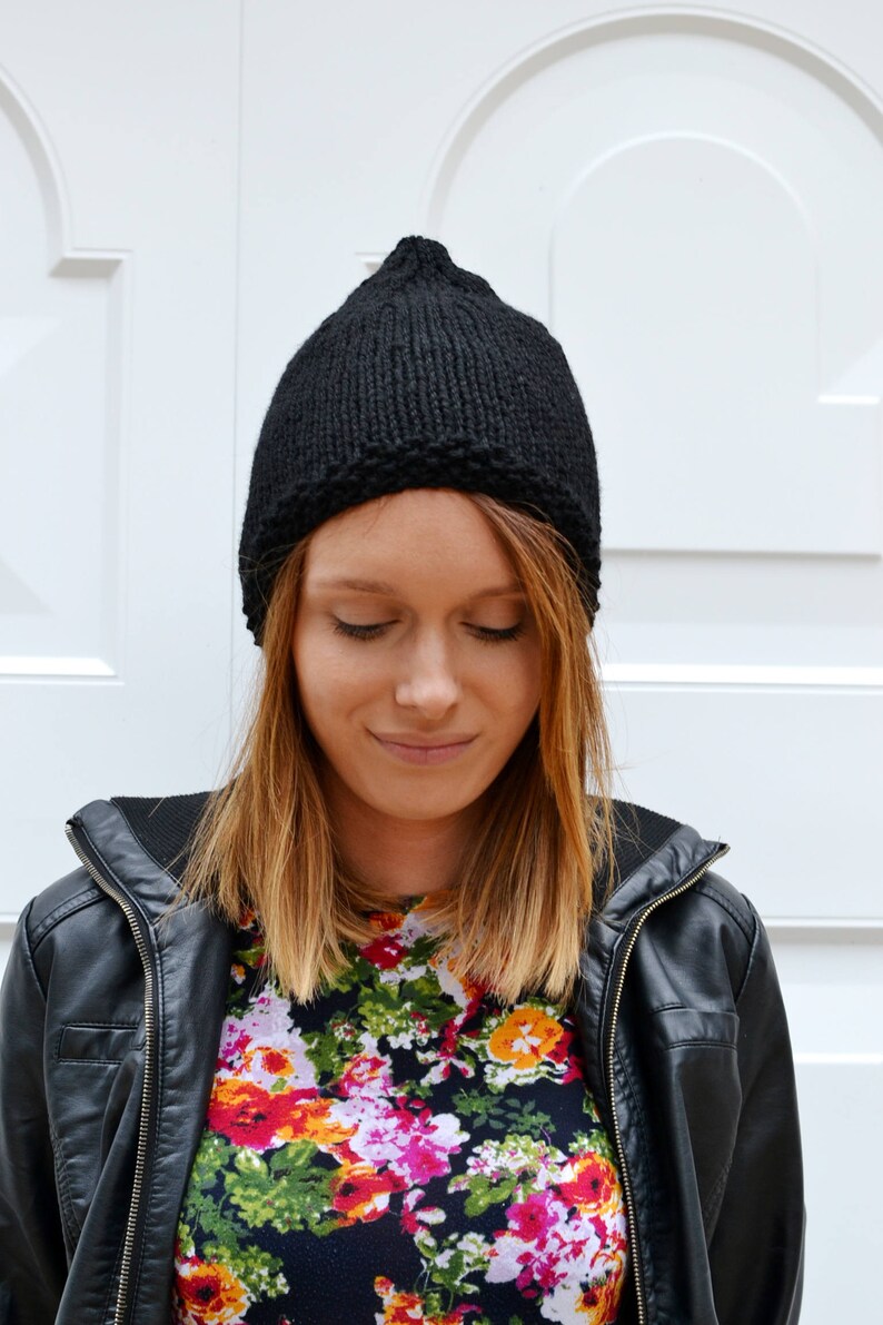 Op de afbeelding: Een vrouw draagt ​​een zwarte gebreide beanie, een shirt met bloemenprint en een zwart leren jack.