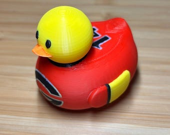 May include: A red rubber duck with a yellow head and black eyes. The duck has a black and yellow design on its body.