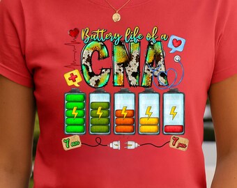 May include: Red t-shirt with the text "Battery life of a CNA" in a colorful design. The design includes battery life indicators, a stethoscope, and a heart. The shirt also has the time 7 am and 7 pm.