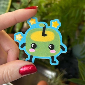 May include: A green and yellow cartoon character with a stem on top of its head. The character has large eyes and a small mouth. It is surrounded by blue and yellow stars.