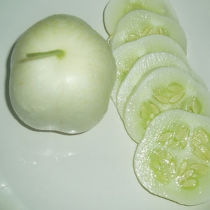 May include: A white, round melon next to a pile of thinly sliced cucumbers. The cucumbers are light green and have visible seeds.