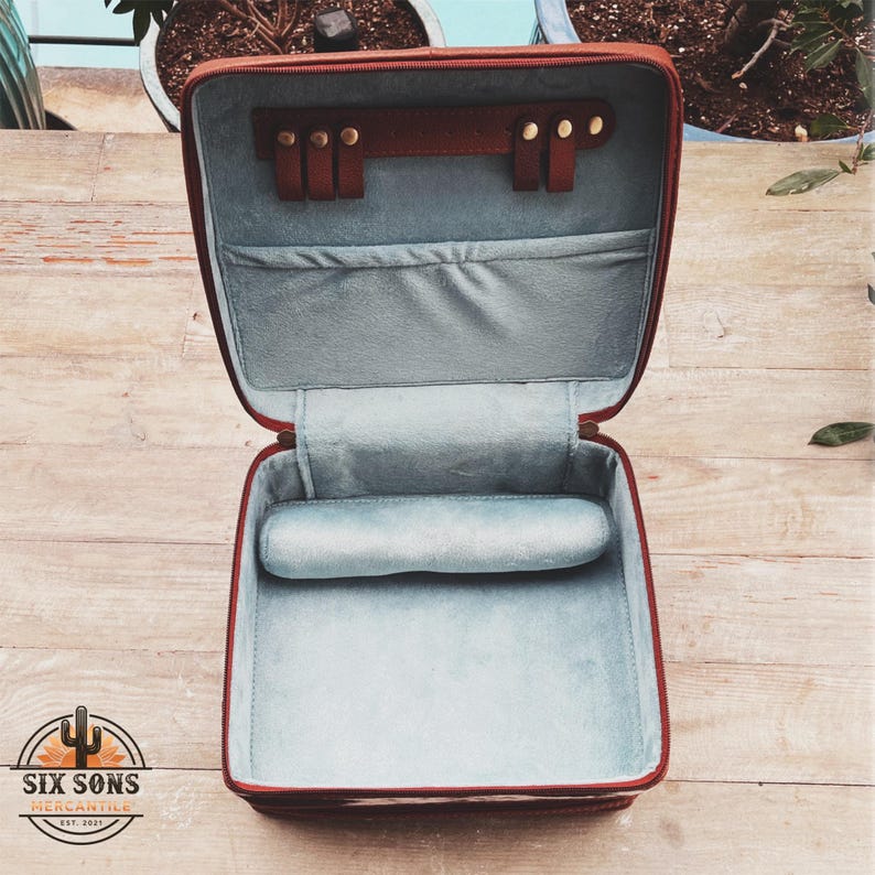 May include: A brown leather jewelry box with a blue velvet interior. The box has a hinged lid and a removable cushion. The lid has a leather strap with gold metal studs.