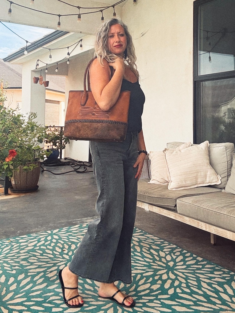 Puede incluir: Un bolso tote de cuero estructurado con un dise&ntilde;o bicolor que presenta una secci&oacute;n superior en color tostado claro y un panel inferior texturizado en marr&oacute;n oscuro. Incluye patrones de costuras blancas y un detalle de borde de cuero trenzado.