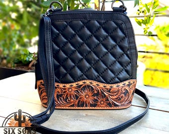 Op de afbeelding: Zwarte quilted lederen schoudertas met een bruine gegraveerde lederen rand met een bloemenmotief. De tas heeft een lange verstelbare schouderband.