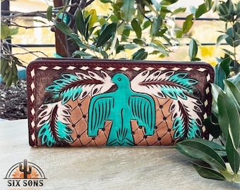 Puede incluir: Una cartera de cuero marrón con un diseño de pájaro turquesa y blanco. La cartera tiene un borde cosido y un patrón de diamante.